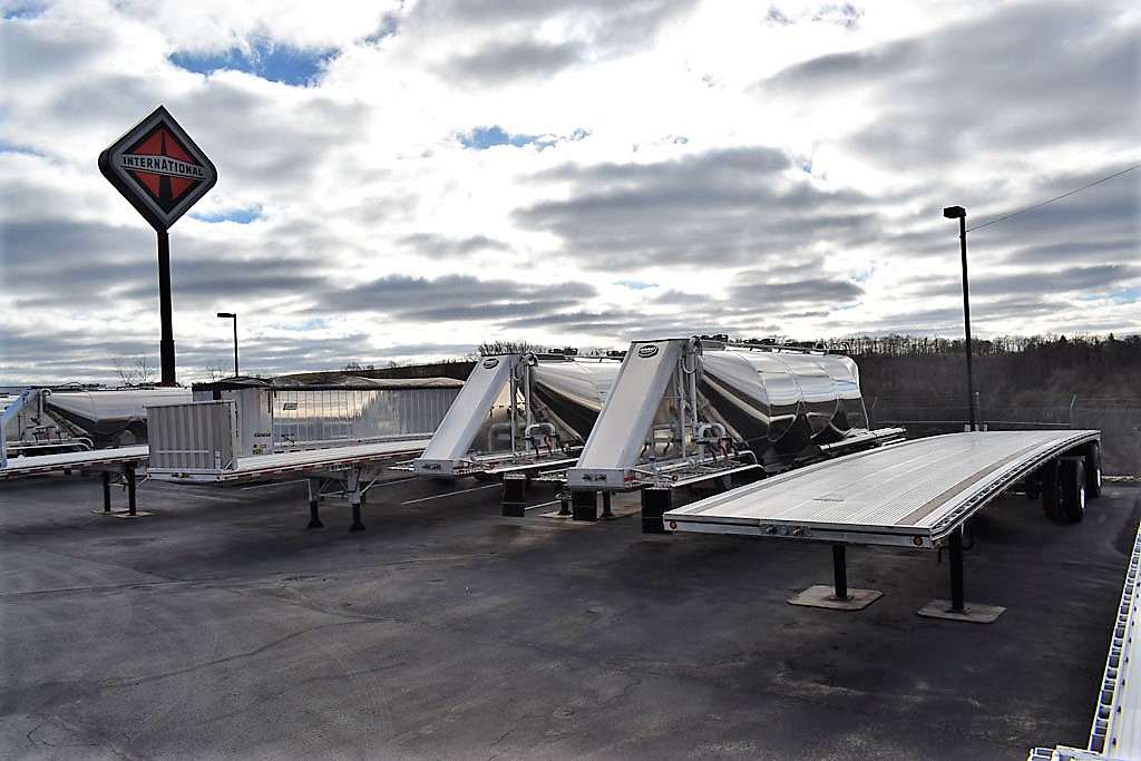 Flatbed and tanker semi trailers sitting in a lot outside at Hill International Trucks