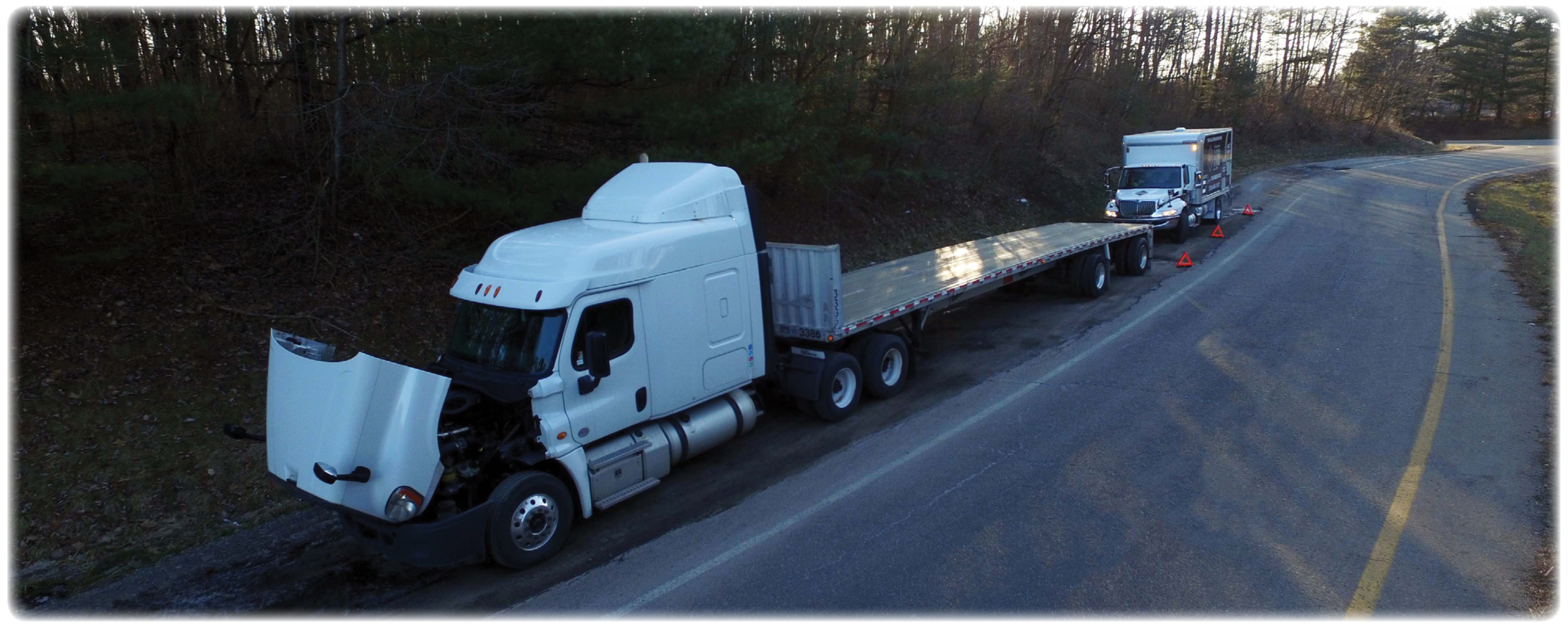 White truck with an open bed and an open engine hatch parked on the side of the road in front of a Roadside Assistance truck.