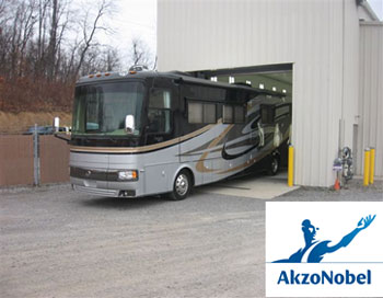 Black, gray, & yellow-striped motorhome exiting the garage of the truck body repair shop.