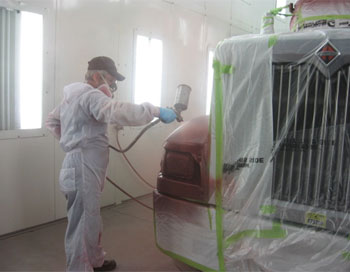 Body repair shop technician wearing a mask working on a red & white truck with plastic film over it.