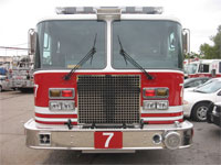 Front-facing fire truck parked in a lot surrounded by other cars on a cloudy day.