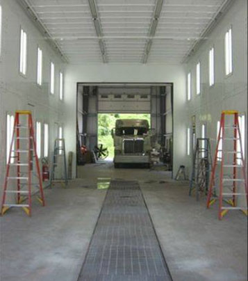 White hallway with concrete floor facing entrance to the truck collision center with a truck inside and an open door.